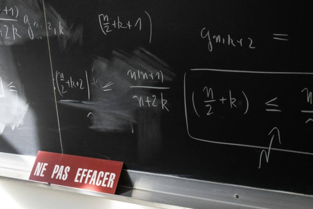 Chalkboard with math equations and French warning sign in a classroom setting.