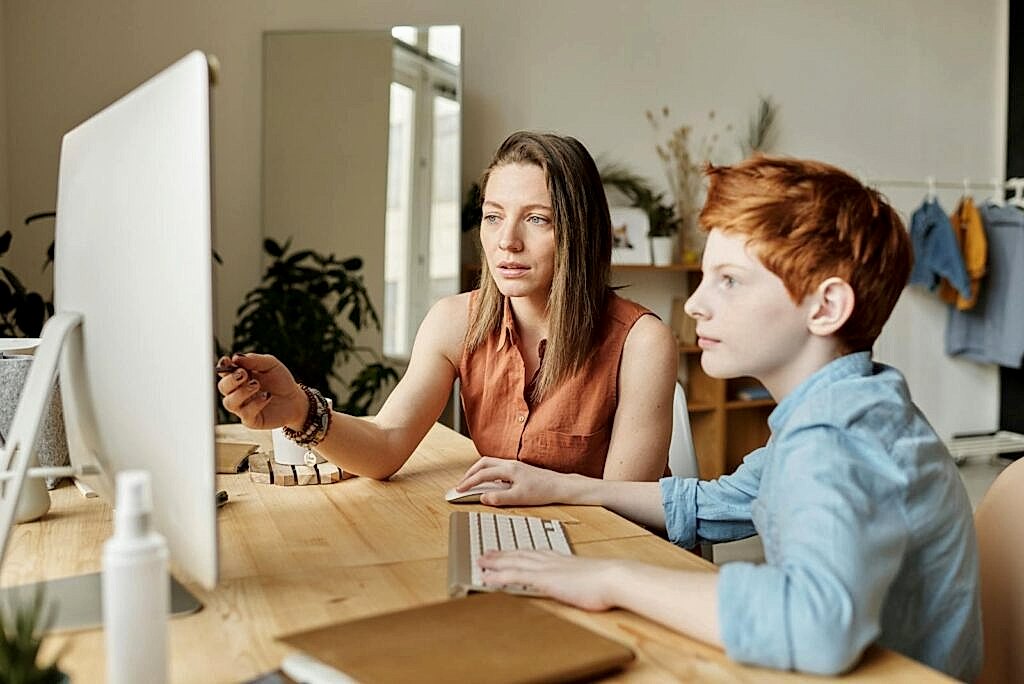 A mother and her son attentively engaged in online learning at home on a computer.